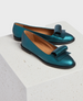 A pair of metallic teal loafers with a glossy finish, featuring a distinctive oversized bow on the front, a rounded toe, a low black heel, and a tan interior lining. 1