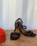 The Coclico Solomiya Heel in Black leather sitting on a table next to orange art. 9