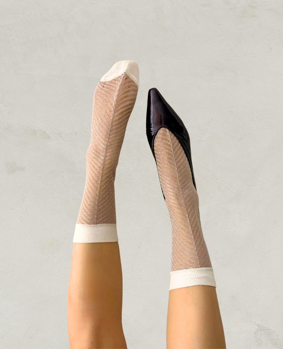 Beige fishnet stockings with white bands worn by a person on a plain background