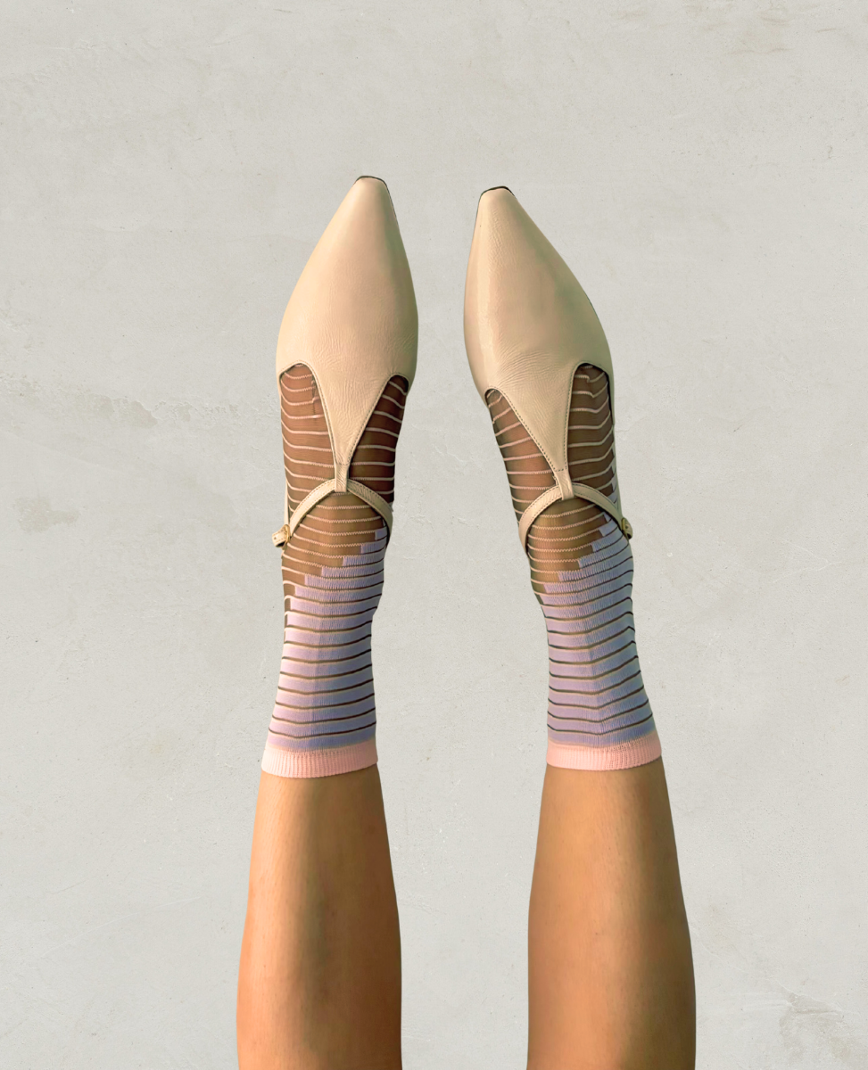 Beige ballet flats worn with striped socks on a plain background