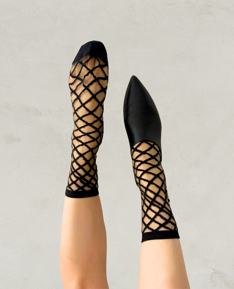 Black fishnet stockings with mesh pattern worn by a person on a light gray background