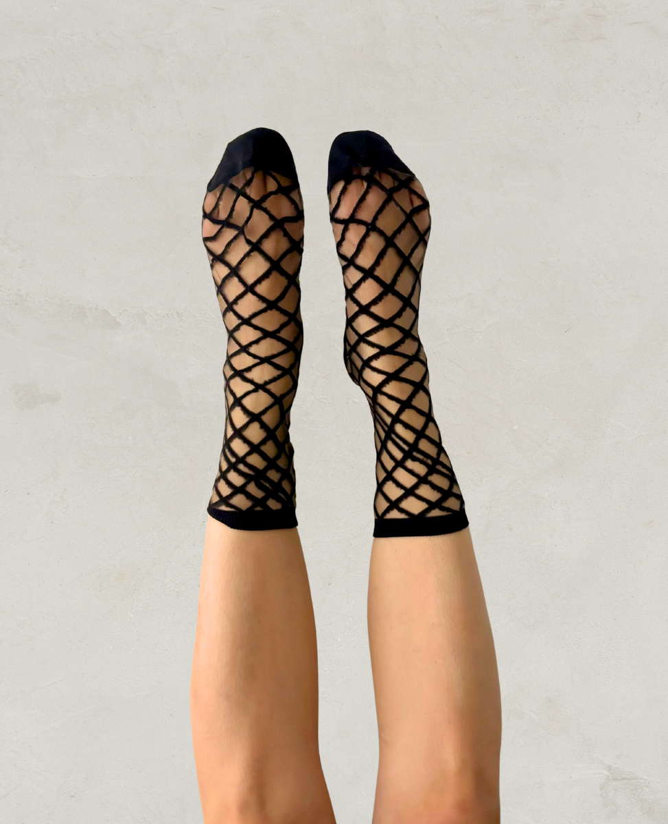 Black fishnet stockings worn by a person on a light gray background