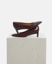 Brown high-heeled shoe on a light gray pedestal against a white background 4