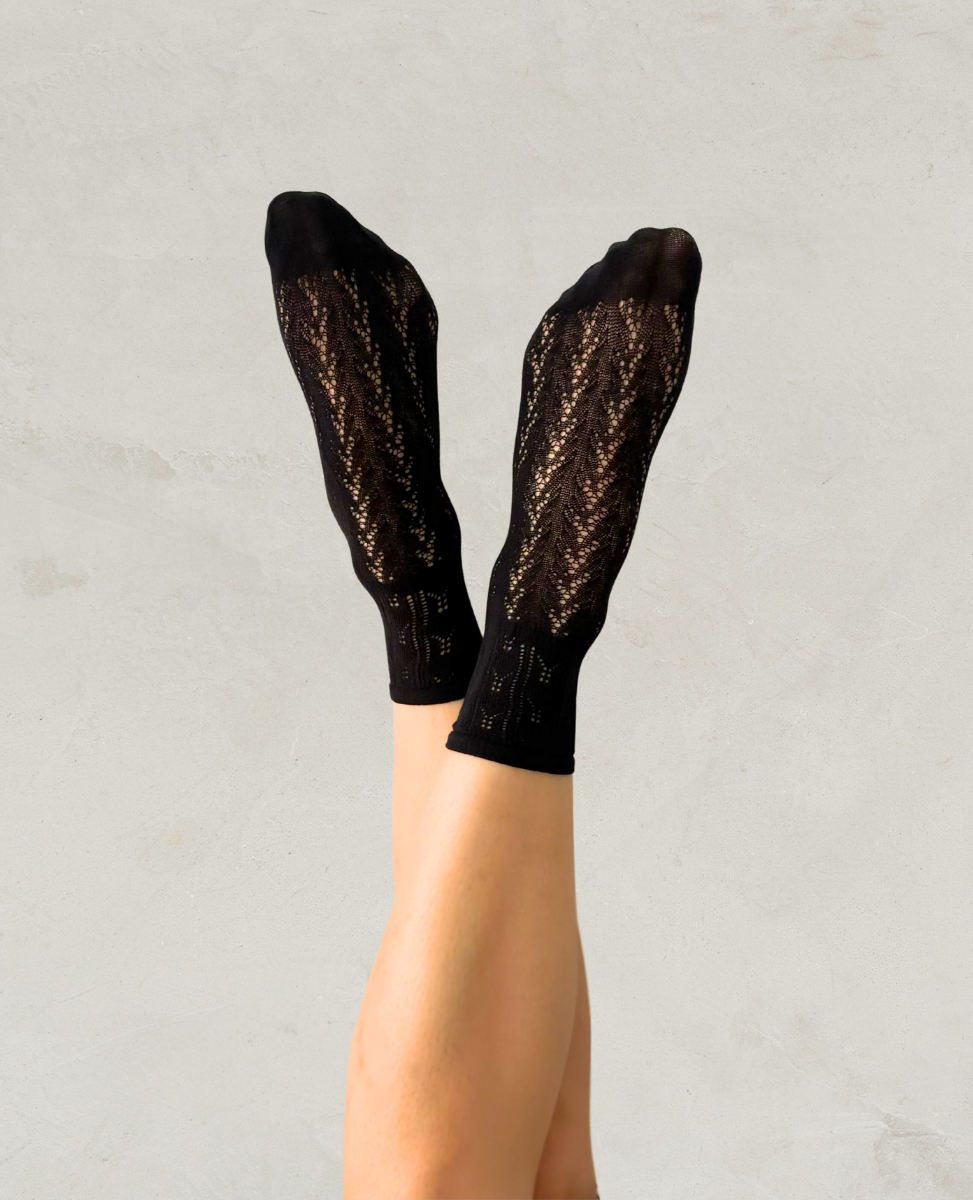 Black crochet socks by Swedish Stockings worn by a person on a light gray background
