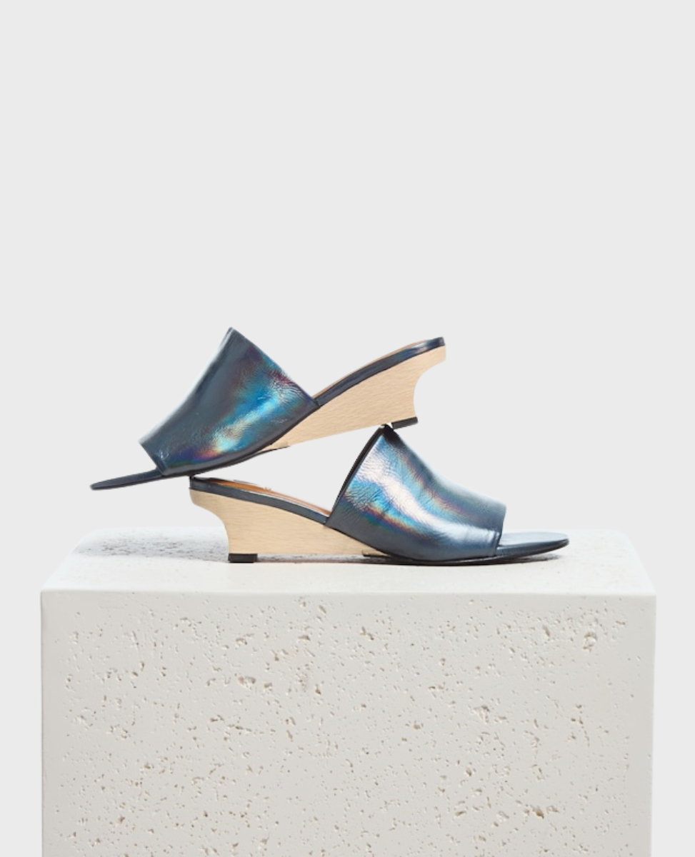 A pair of sleek, iridescent black open-toe mules with a smooth leather upper, featuring a unique wooden wedge heel and a minimalist design.