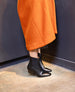 A pair of sleek, black leather ankle boots with a squared toe, low block heel, and elastic side panels, worn with an orange wool coat. 6