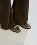 Bronze metallic loafers with a sleek, shiny finish and a distinctive oversized bow detail on the top, paired with dark brown corduroy pants. 2