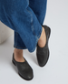 Black slip-on shoes with a smooth, matte leather finish, rounded toe, and elasticized opening, worn with blue denim jeans. 3