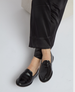 Shiny black leather loafers with a sleek, smooth texture and a low heel, worn with black satin pants. 3