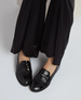 Shiny black leather loafers with a smooth, glossy finish and a low heel, worn with black wide-leg pants. 4