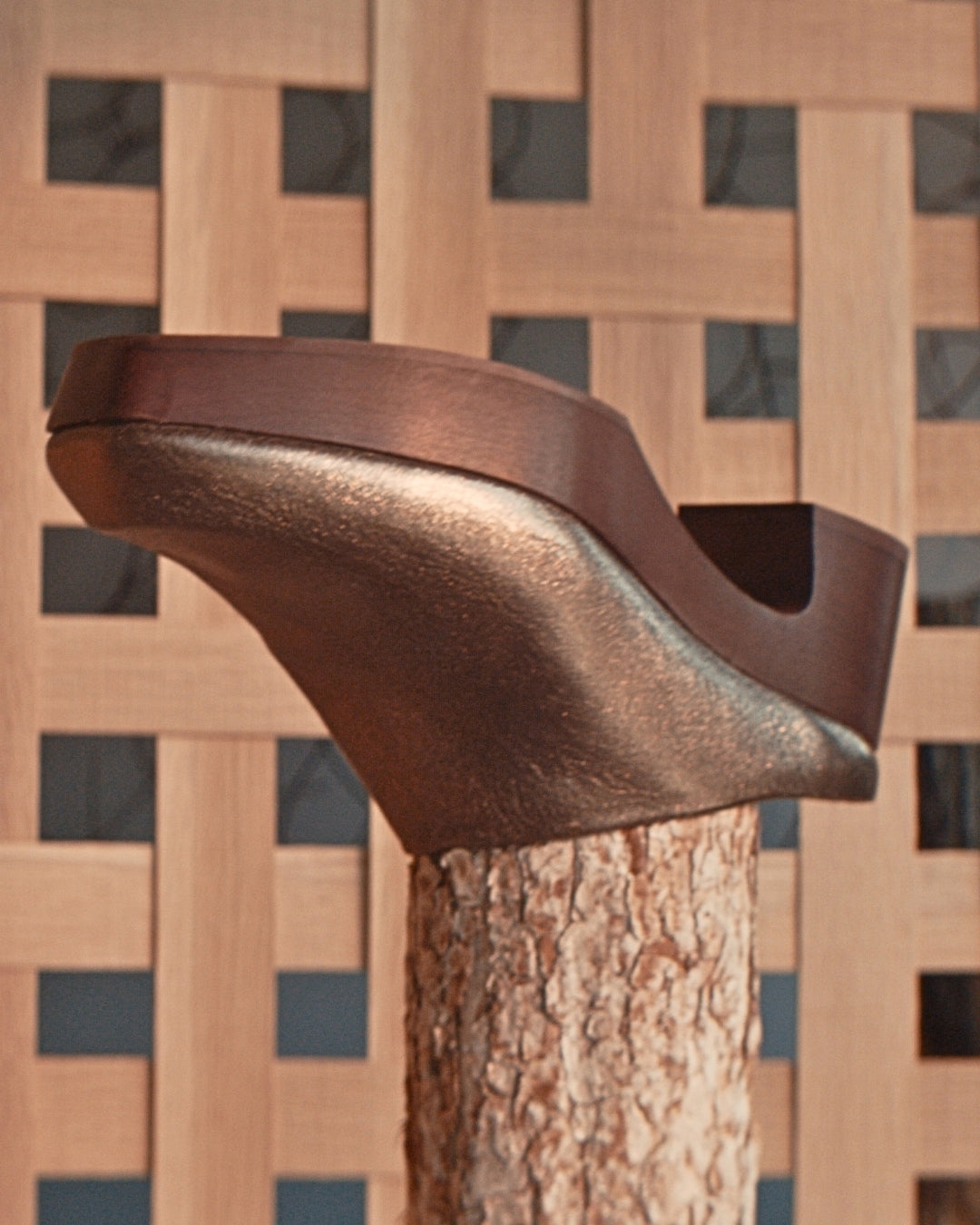 Coclico Quilla Clog in Bronze crinkled metallic leather balanced on a tree stump against a wooden lattice screen