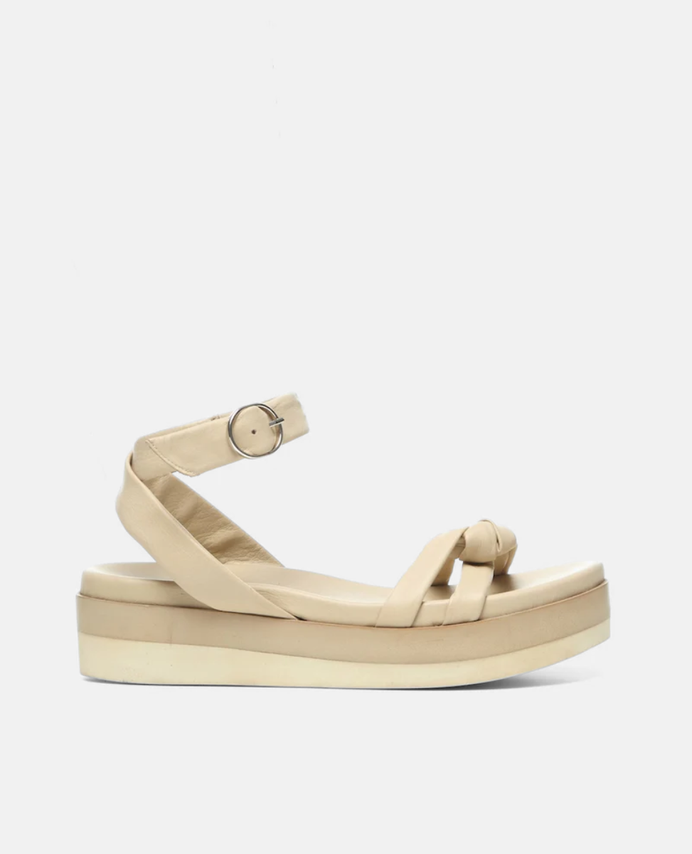 A beige sandal with a thick platform sole, featuring a crisscross strap design and an ankle strap with a silver buckle, made from smooth leather material.