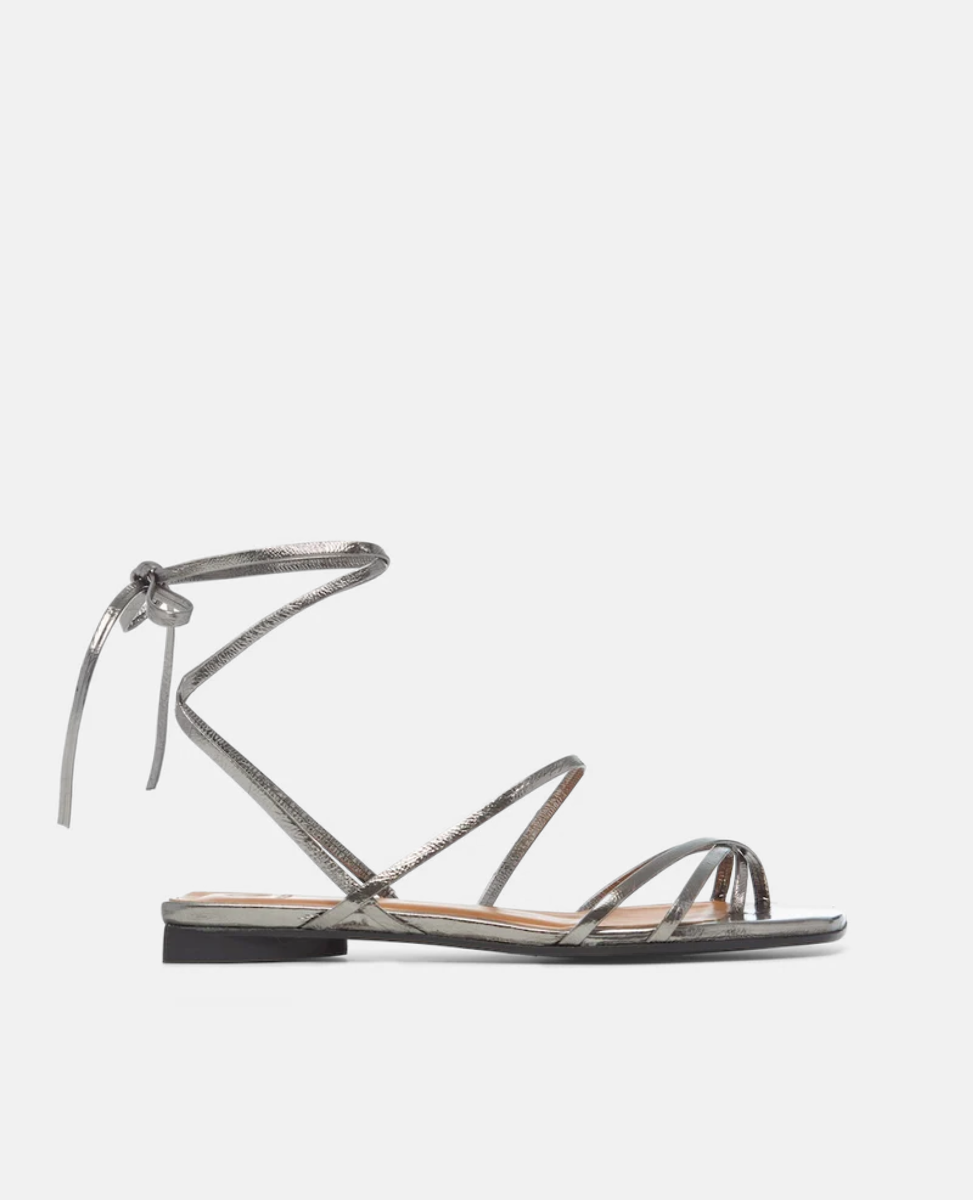 A sleek, metallic silver sandal with thin, crisscrossing straps and a delicate ankle tie, featuring a flat sole and minimalist design.