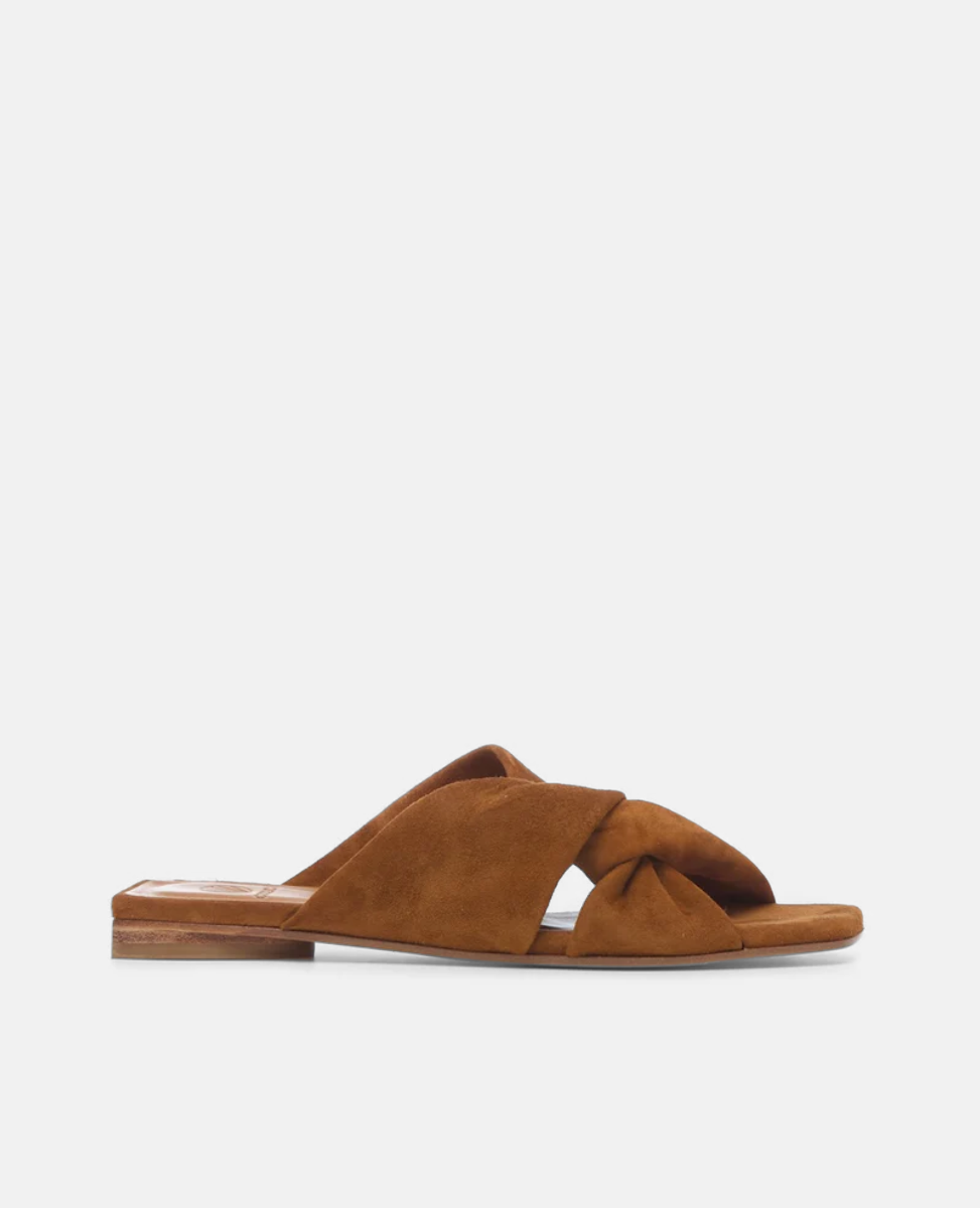 A brown suede sandal featuring a flat sole, crisscross straps with a knot detail, and a minimalist design.