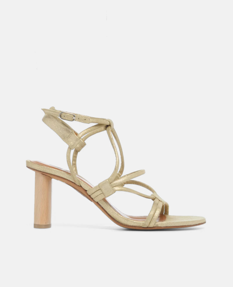 A gold high-heeled sandal with a wooden block heel, featuring thin, intertwined straps and an adjustable ankle buckle.