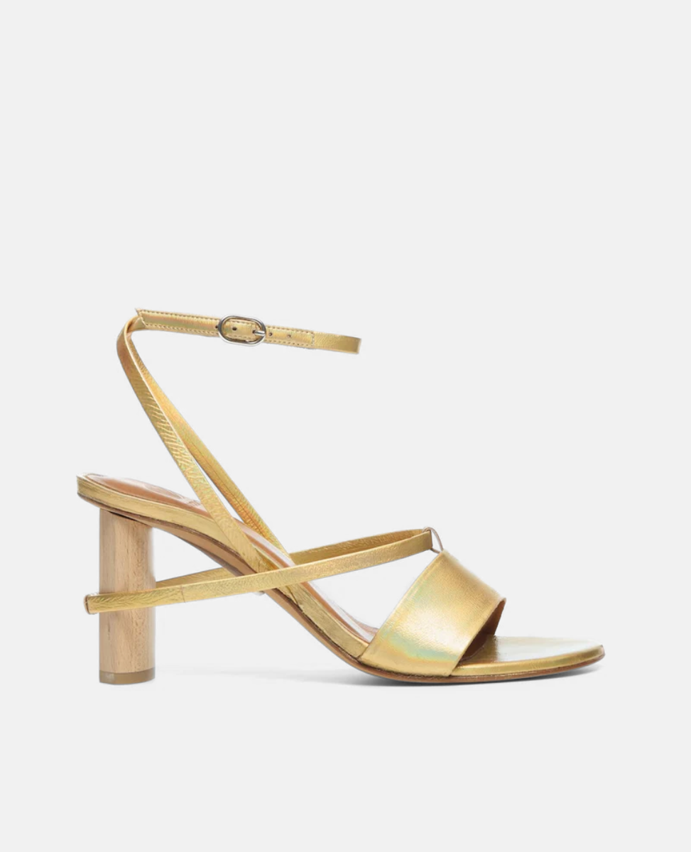 A sleek, gold sandal featuring a minimalist design with thin straps, an adjustable ankle buckle, and a unique cylindrical wooden heel.