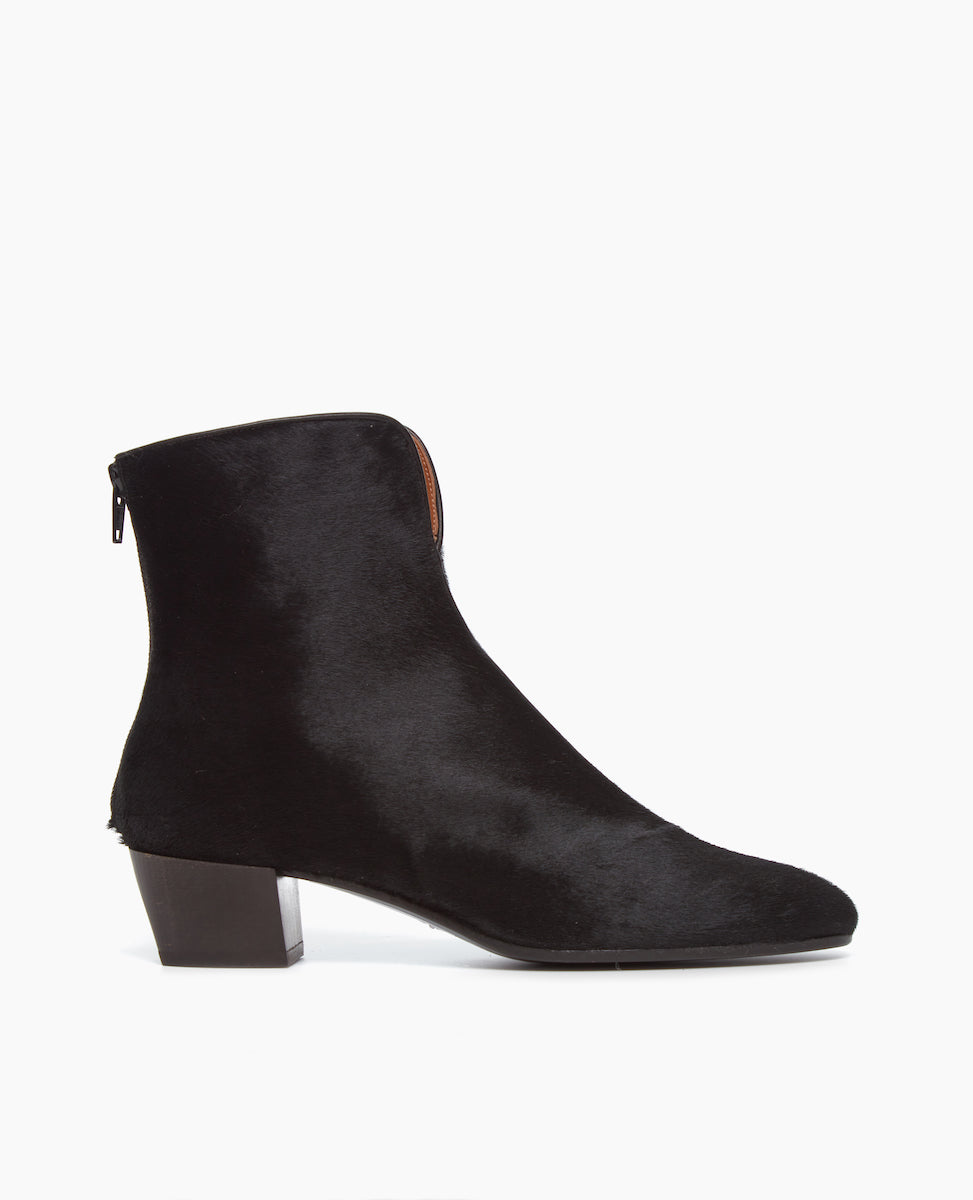 Side view of the Coclico Celia Boot in spanish crinkled patent suede: raised piping up the center, mirrored by the clean look of a back-zip, and accentuated by a flattering V-shaped topline with a solid angular wood heel.