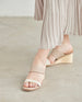 Close up of model in an open a two-neutral-toned slide, asymmetric straps, solid wood mid-height wedge. 6