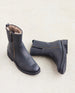 Durum Shearling Boot displayed from the front in black leather. This boot features an upper updated lug sole. It is an elevated moto boot featuring an outside zip closure and a full shearling-lined interior. Left boot is lying on the floor. 13