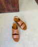 The Coclico Everly woven sandal on a concrete floor with a wood door behind. 2