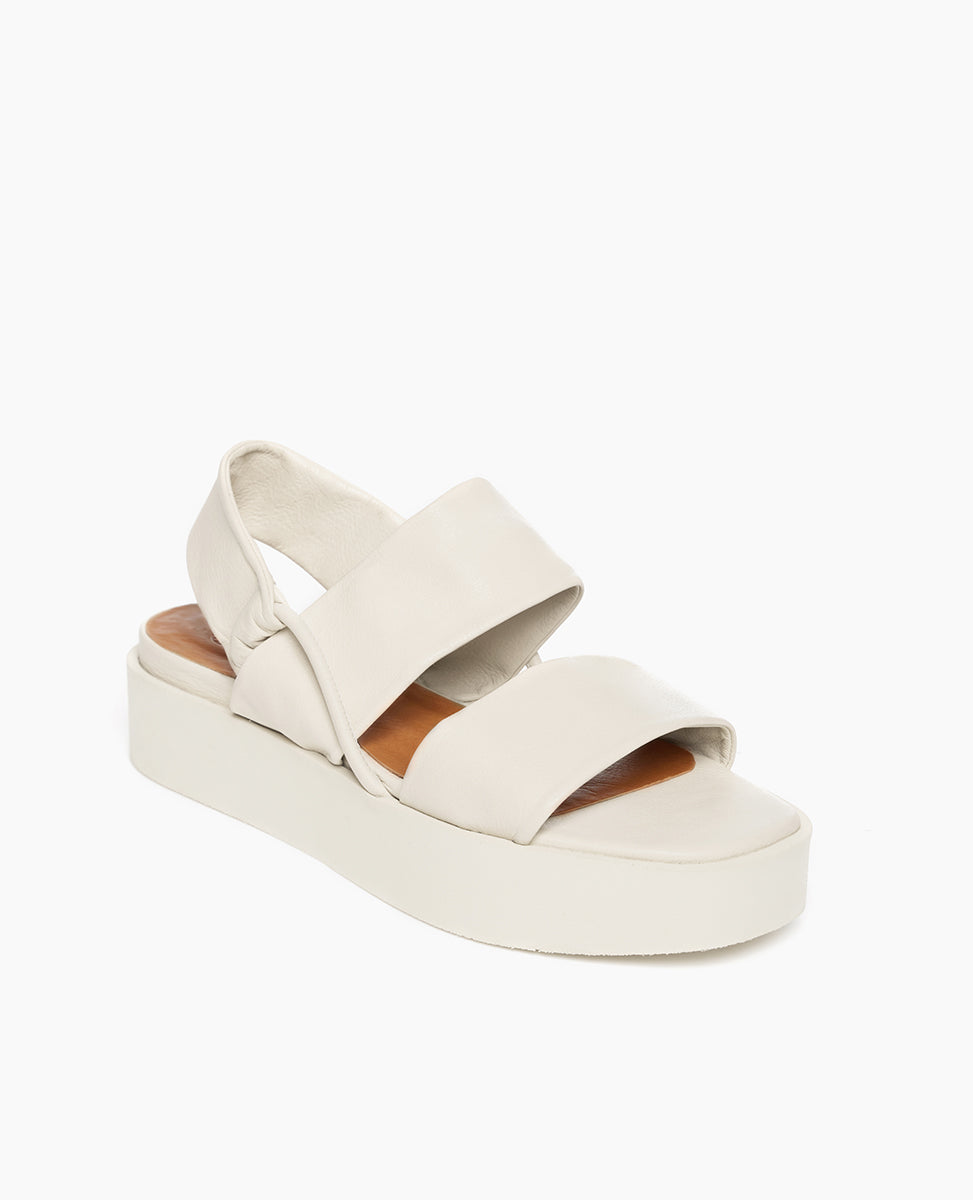 Coclico Imna Wedge in Greige leather, angled view: an open wedge with 2 tubular straps across foot, elasticated slingback strap, mid-height EVA  flatform sole.