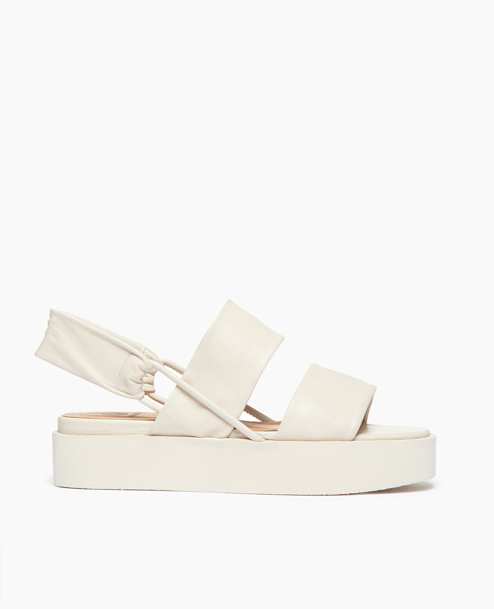 Side view of Coclico Imna Wedge in Greige leather: open wedge with 2 tubular straps across foot, elasticated slingback strap, mid-height EVA  flatform sole.