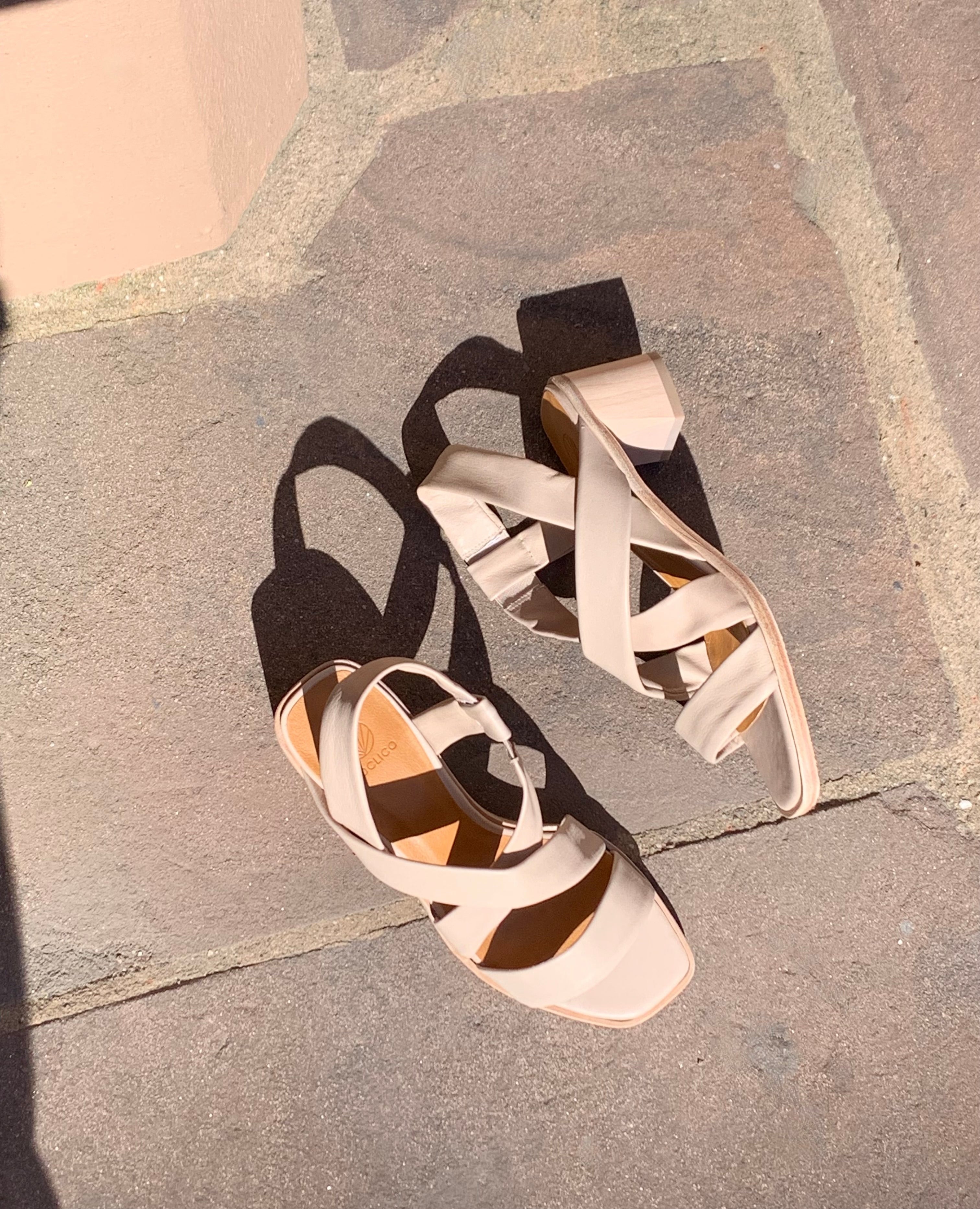 A Coclico open slip on sandal with leather tube straps across the foot, sling-back strap, wood block mid-height heel. 