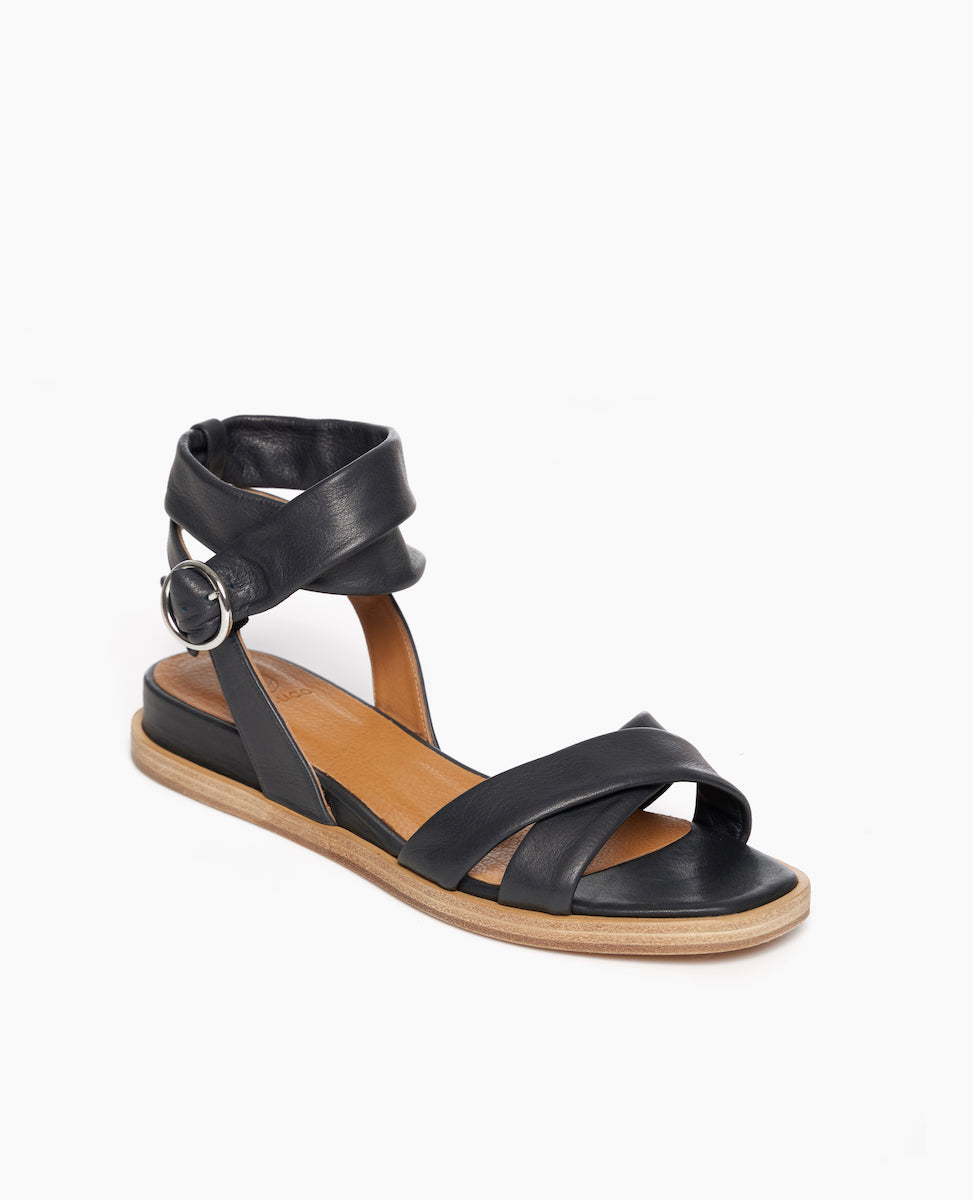 Coclico Katriane Sandal in Deep Sea leather, angled view:open sandal with tubular straps across foot and ankle, round buckle closure, slight leather wrapped wedge. 