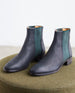 Angled side view of the Coclico Medlar Boot in Black placed on a wool stool.  3
