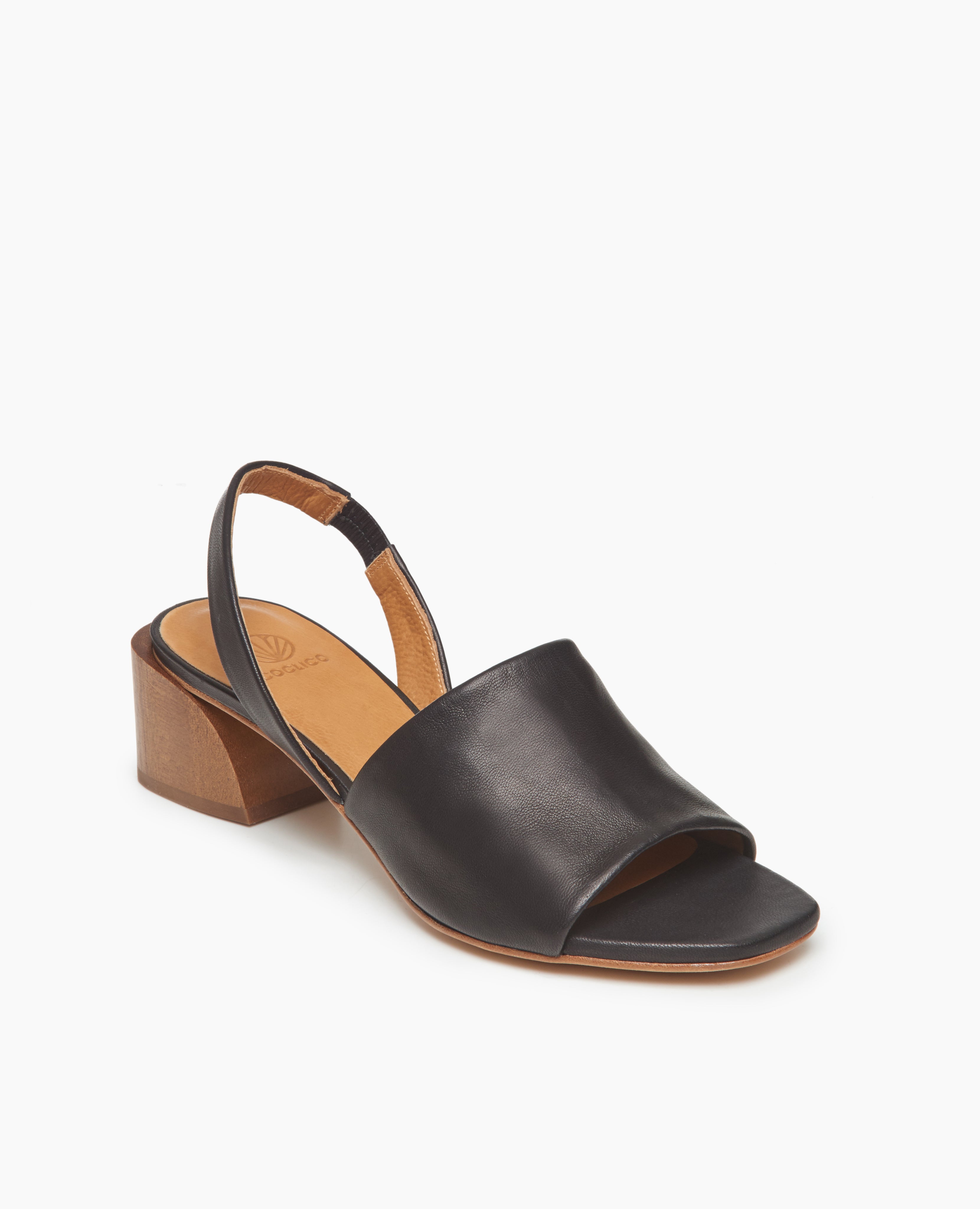Coclico Okolo Sandal in Black leather, angled view: slingback sandal with wide stretch leather band across the foot and softly curved, low, solid wood heel. 