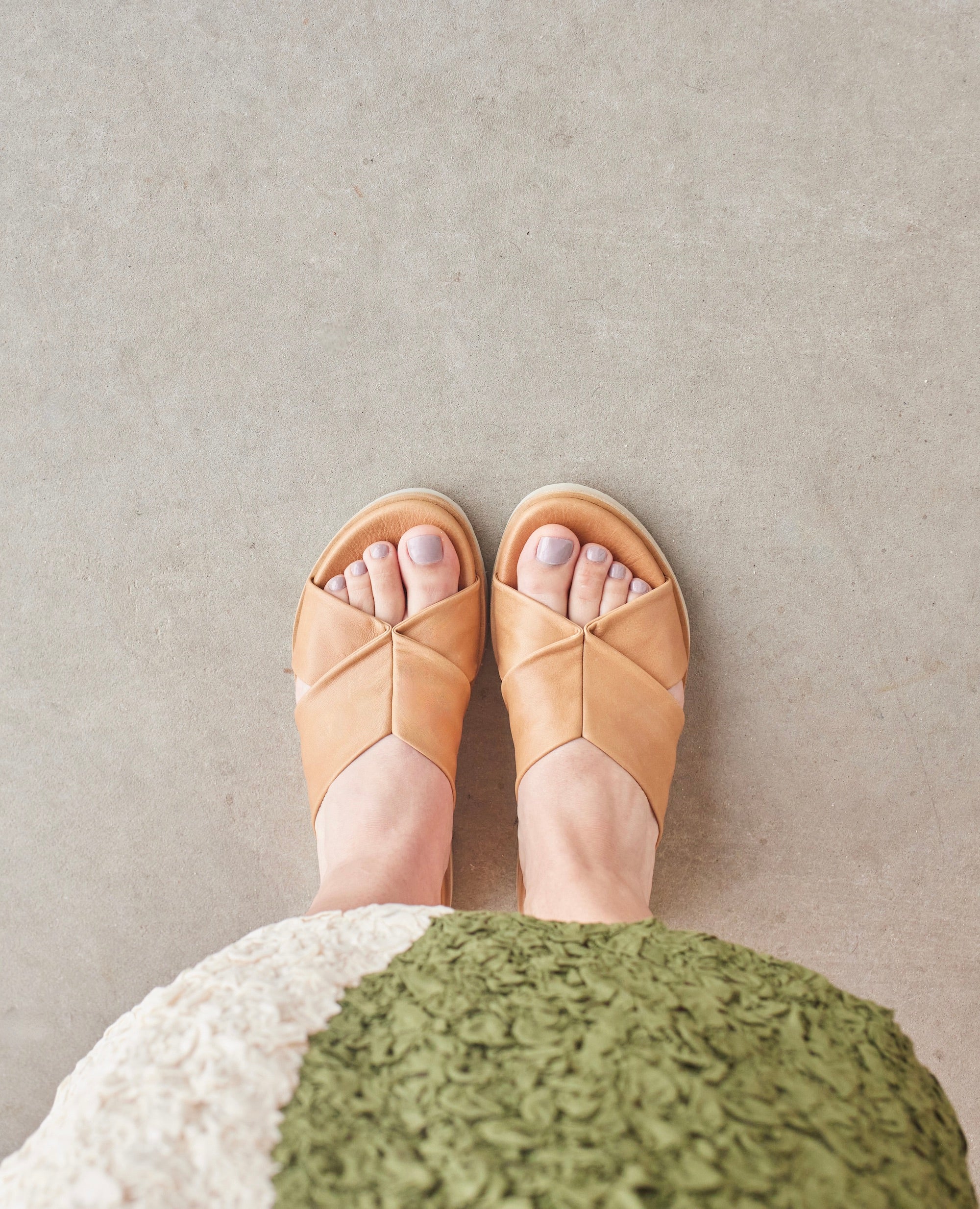 Top view shot of model wearing the Coclico Pasque Sandal in Mandorla  leather: a low pine wedge slide sandal, intertwined leather tube straps across foot, gum-rubber sole.