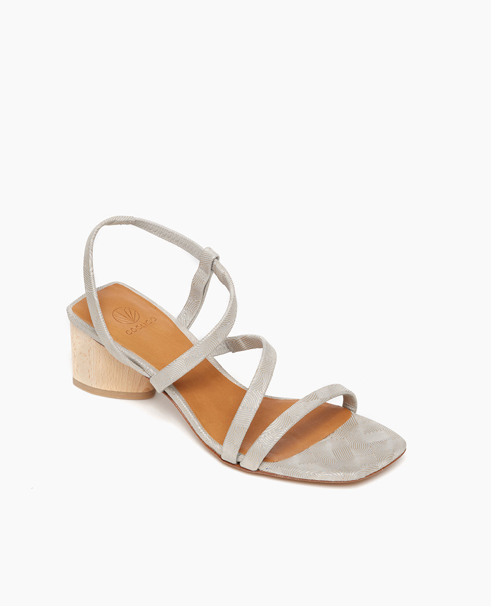 Angle view: Coclico Shirin Heel in Platino Emboss leather: an open sandal with textured leather asymmetrical string-like straps across foot, solid mid-height wood heel. 