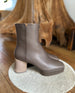 Side view of the Travis Boot in Taupe on a white rug with wood in the back.  5