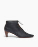 Side view of the Waffles Bootie in Black Leather; featuring a softly arched solid wood heel and gathered tie at the ankle revealing just enough to be both feminine and practical. 1