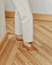 Model wearing the Coclico Alskling Flat in Luggage leather:  an elasticated top line that hugs the foot, two-part .5 inch EVA sole, squared-off toe - on wood flooring, top view. 3