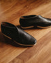 Coclico Arro Flat in Black leather: slip-on flat with stretch leather that hugs foot, white two-part .5 inch EVA sole and a squared-off toe close up, sunlit shot on wooden flooring.   8