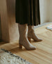 Model in Coclico Basil Boot in Limestone nubuck a tall boot with a mid-height wood block heel and inside zip closure - on wood flooring.  4