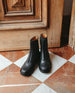 Pair of Coclico Dal Boot in Black leather on glossy red and white marble flooring with a wood door behind.  6