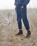Lower half of a women wearing a casual blue top and pants along with the Hop Boot in Deep Sea  while standing outside. 7