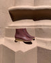 Side view of the Coclico Java Boot in Merlot leather: Italian certified sustainable leather low-height solid wood wedge, inside zip closure and rounded toe - placed on a terracotta pillar.  4