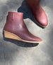 An Italian certified sustainable leather low-height solid wood wedge, inside zip closure and rounded toe - Coclico Java Boot in Merlot leather in sunlight.  3