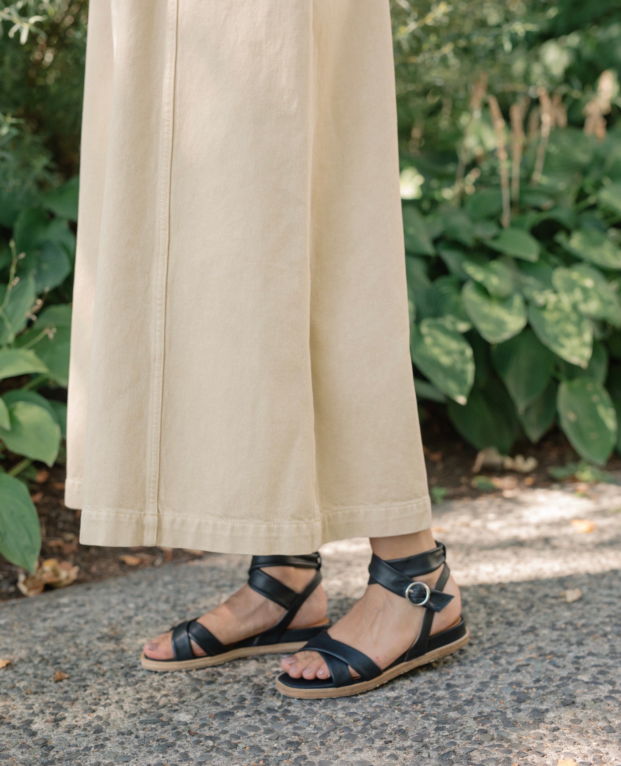 Close up of model wearing Coclico Katriane Sandal in Deep Sea leather an open sandal with tubular straps across foot and ankle, buckle closure, slight leather wrapped wedge. 