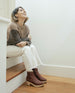 Model sitting on staircase wearing the Coclico Keep Shearling Clog in Britannic leather, a shearling-lined clog with tapered, snipped toe, inside zip closure, mid-height wood block platform.   7