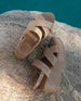 Close up of Coclico Lacine Wedge in Tobacco suede, angled view:a open crisscrossed sandal on a recycled cork wedge platform, back strap and velcro closure -  on a boulder by the pool. 4