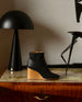Coclico Lodi Boot in Black leather, side view: Solid-wood, sculpted, inset 75mm height wedge with inside zip closure, seam detail on top of foot and rounded toe - placed on the table with decor in background.  2