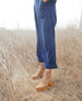 Woman standing in hay modeling a lace-up clog featuring a 3.5 inch solid wood heel, leather sole and inside zip closure - Coclico Vanji Clog in Tobacco suede. 3