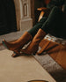 Woman seated modeling the Wakame Boot in Mandorla leather: a sophisticated Coclico pointed-toe boot with a 50mm arched solid wood heel and inside zip closure - close up. 4