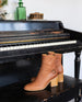 The Babette Bootie in luggage leather on a piano bench. 4