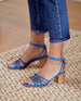 Close up of woman modeling Babs Heel in Blu Estate leather: open sandal with 6 tubular straps across the foot, ankle strap, buckle closure, wood block heel. 6