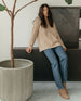 Model leaning against a credenza, styled in jeans, a sweater, and the Bani boot in Tobacco. 8